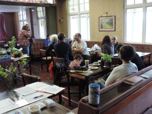 People chatting amongst coffee, plants, books and cakes.